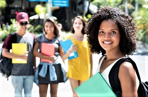 A girl holding a binder. Her three friends are waiting on her in the background.