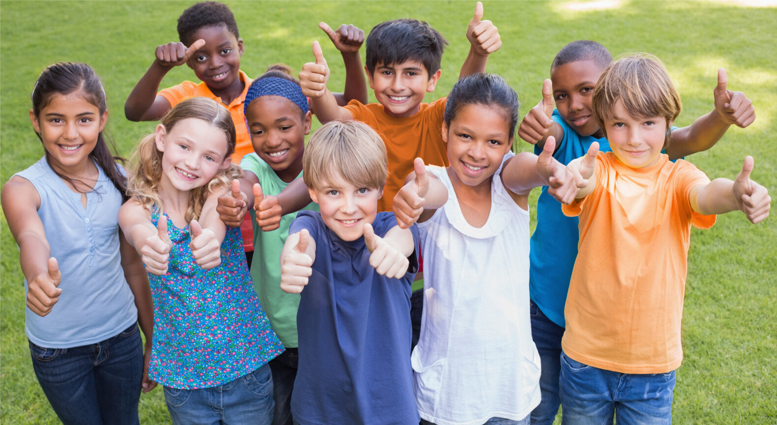 Group of children outdoors giving thumbs up.