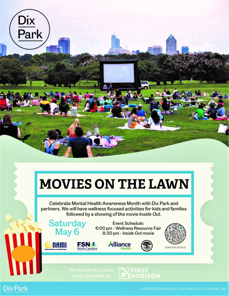 People sitiing on lawn beach towels looking at a large movie screen at a park
